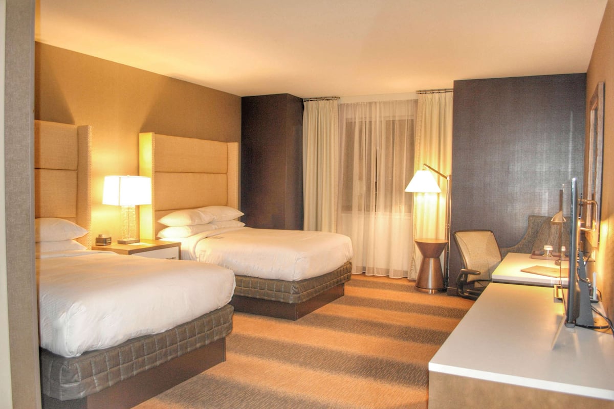 A hotel room with two beds, a desk, a chair, and two lamps.