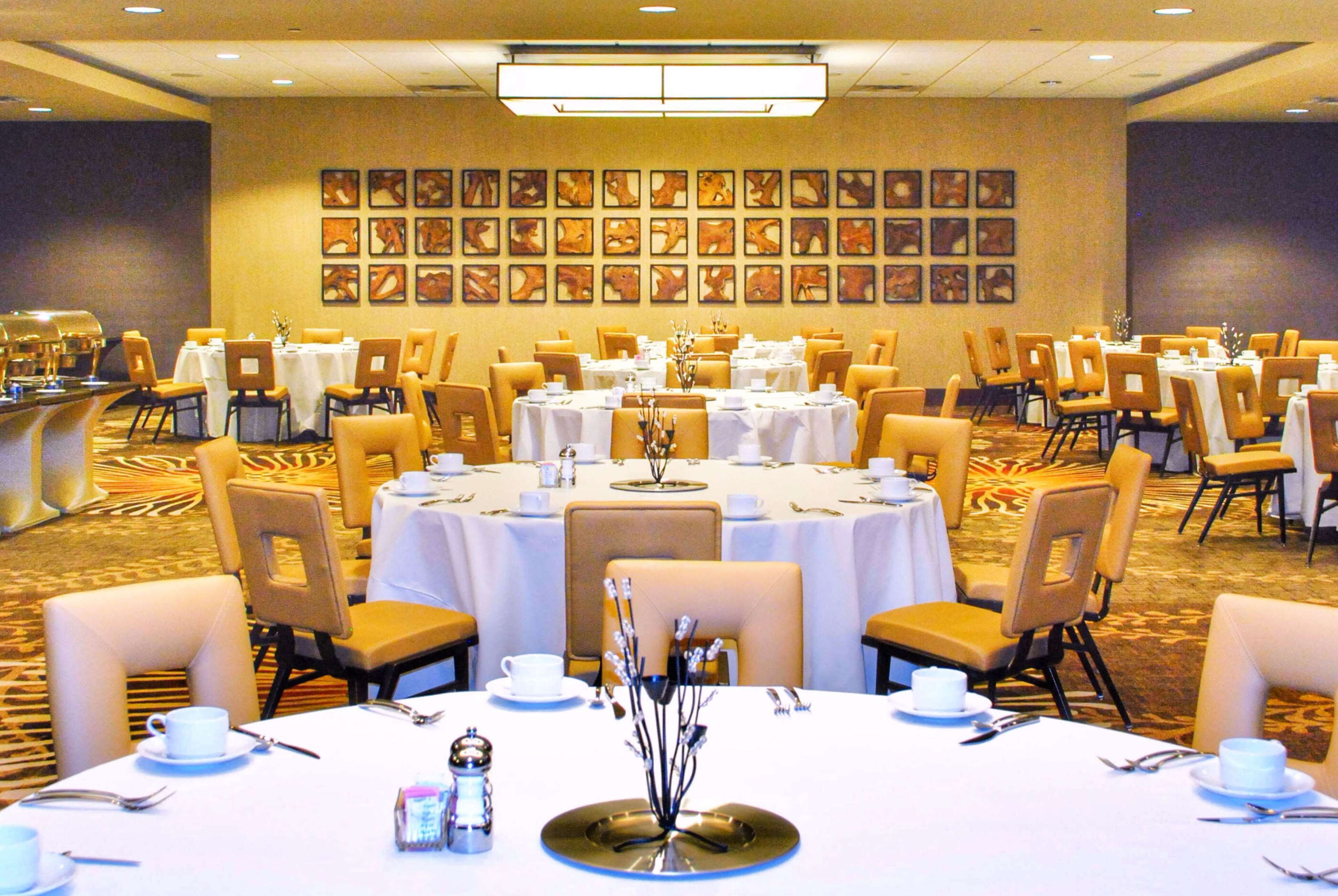 Un salón de banquetes con mesas redondas dispuestas para comer, sillas y una zona de bufé.