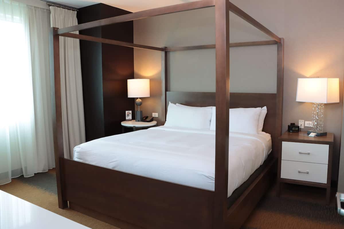 A four-poster bed with white linens, a bedside table with a lamp, and a nightstand with a phone and a small table.