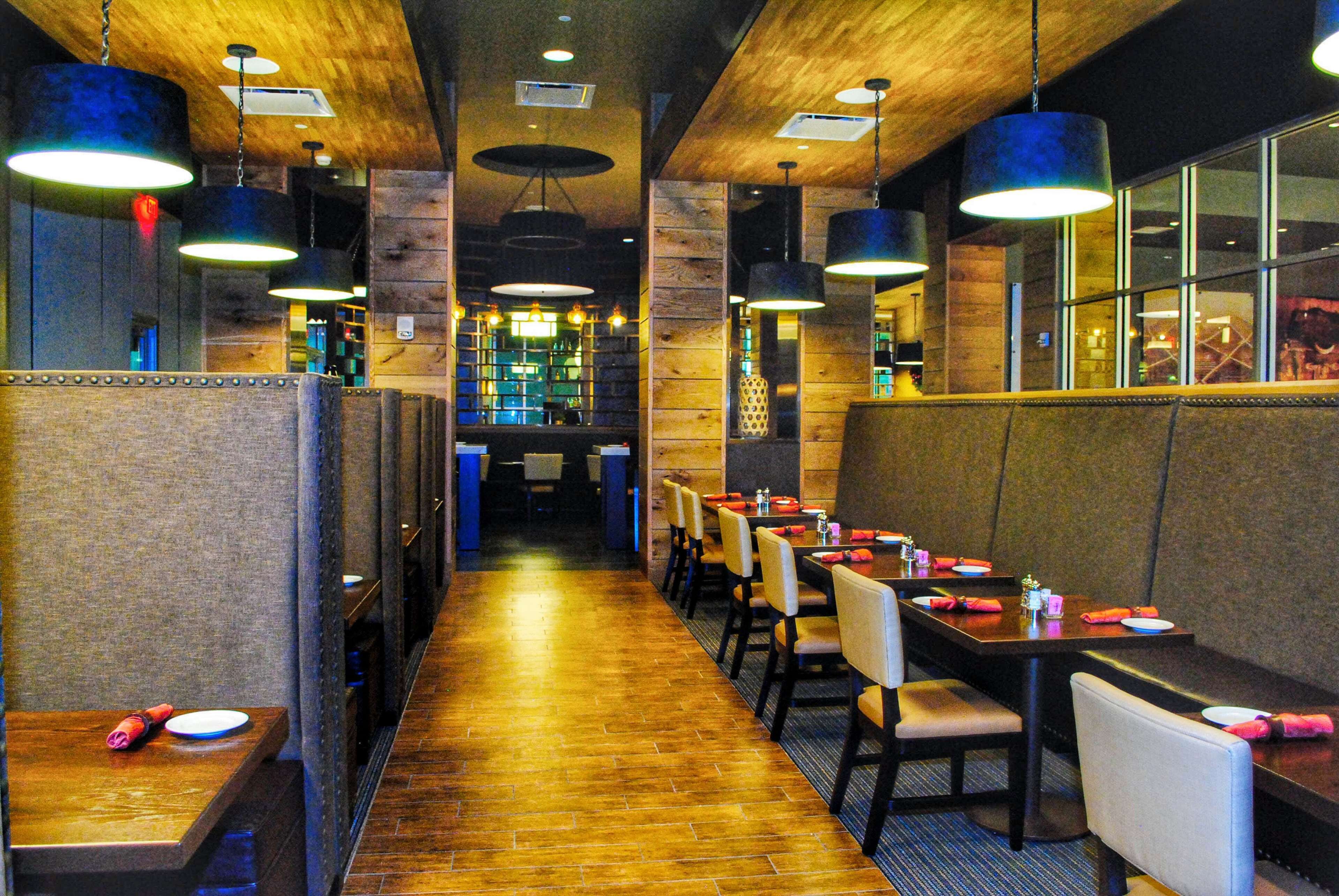 Un restaurante con paneles de madera, lámparas colgantes y una larga barra con mesas y sillas.