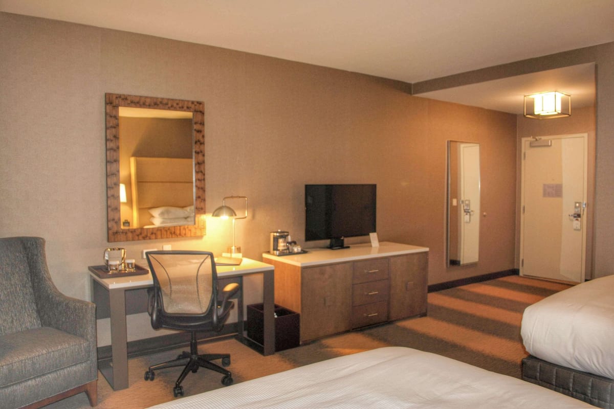 A hotel room with a bed, a desk with a computer, a chair, a television, and a mirror.