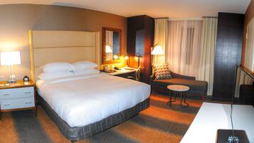 A hotel room with a large bed, a desk, a chair, a small table, and a TV.