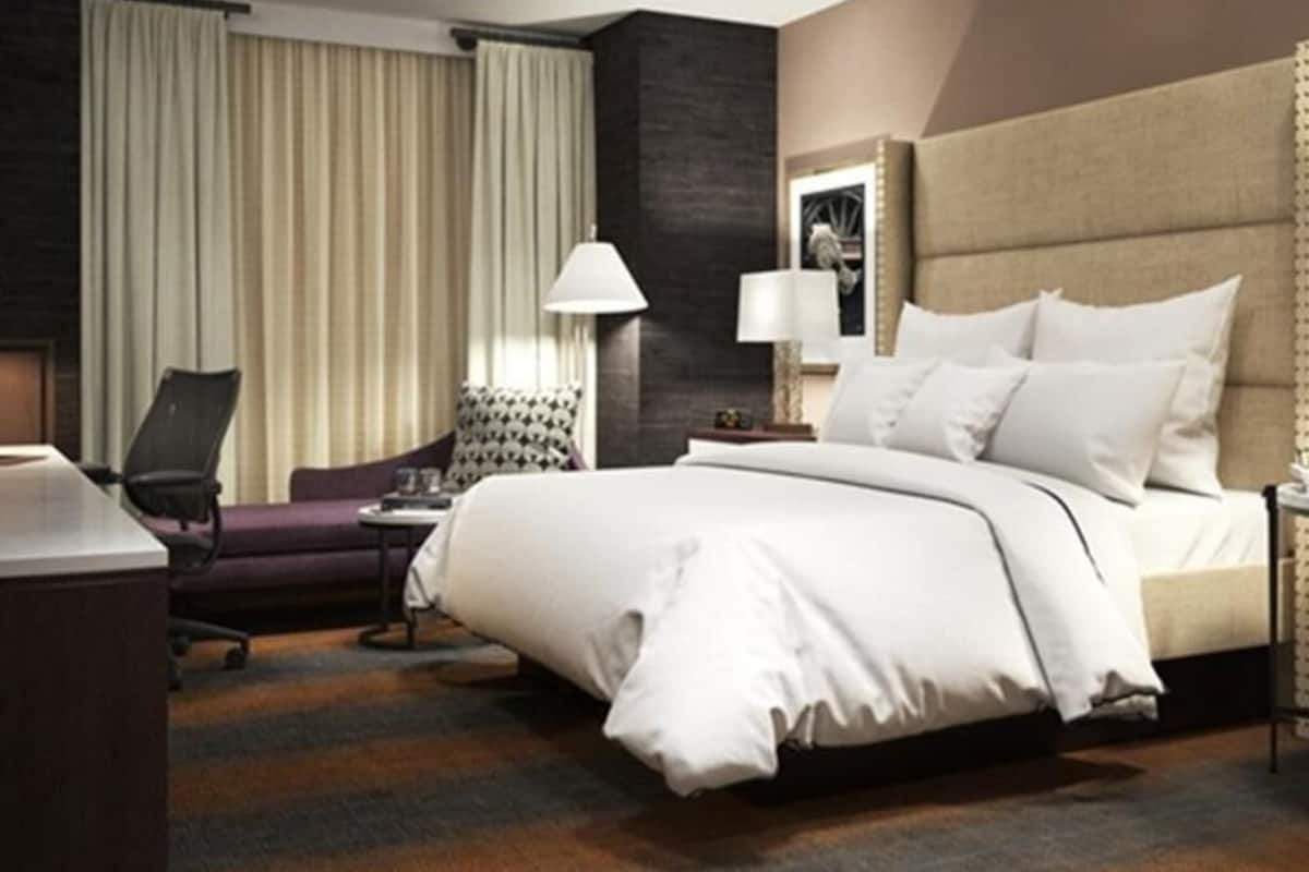 A hotel room with a large bed, a desk, a chair, a lamp, and a window with curtains.