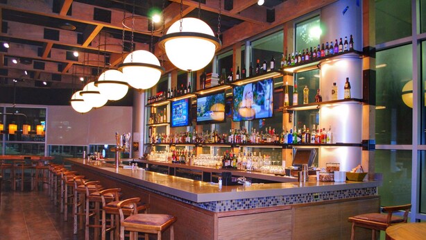 A bar area with multiple seating options, a well-stocked bar counter, and several televisions mounted on the wall. - Doubletree By Hilton Reading (Reading)
