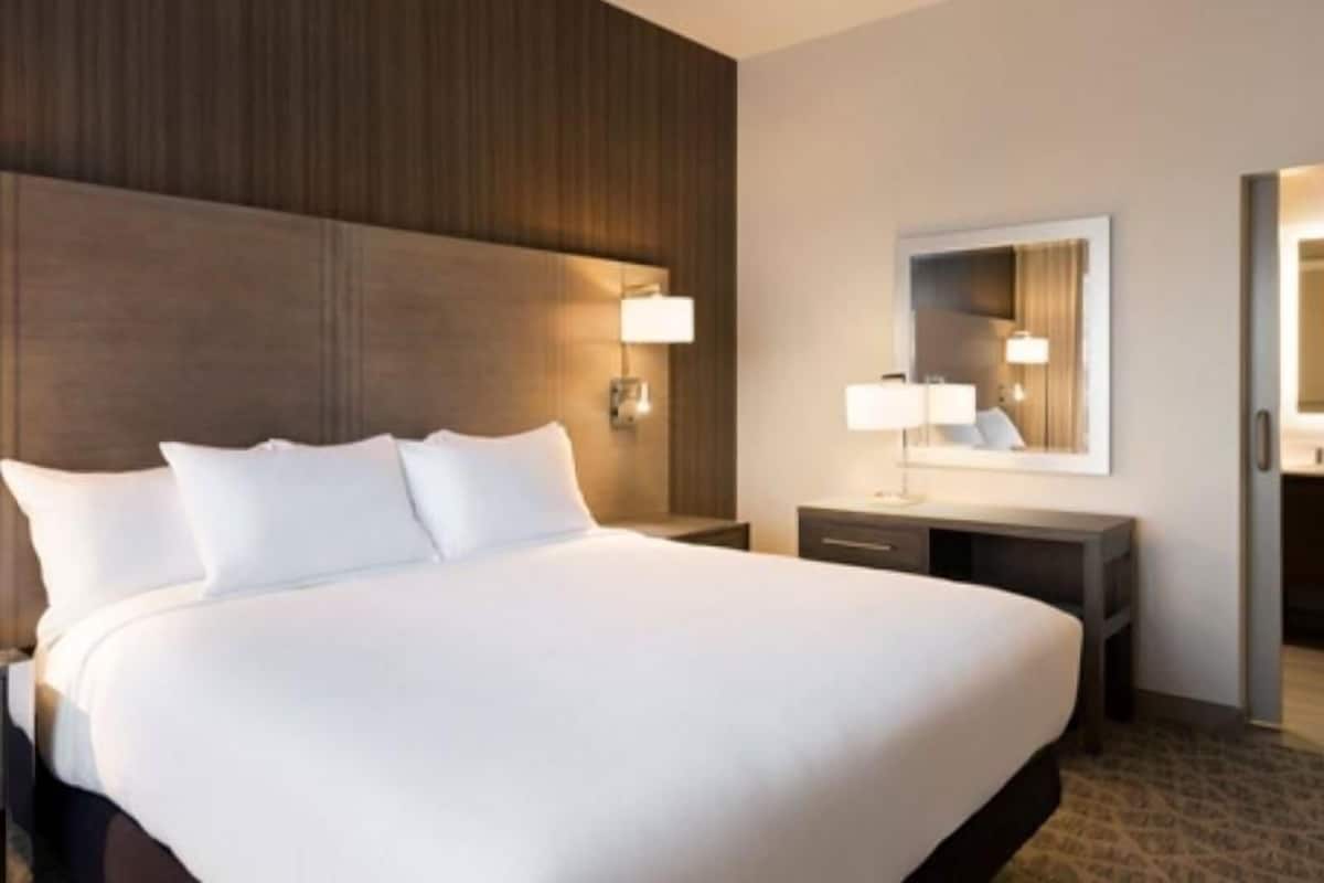 A hotel room with a large bed, bedside lamps, a mirror, and a wooden headboard.
