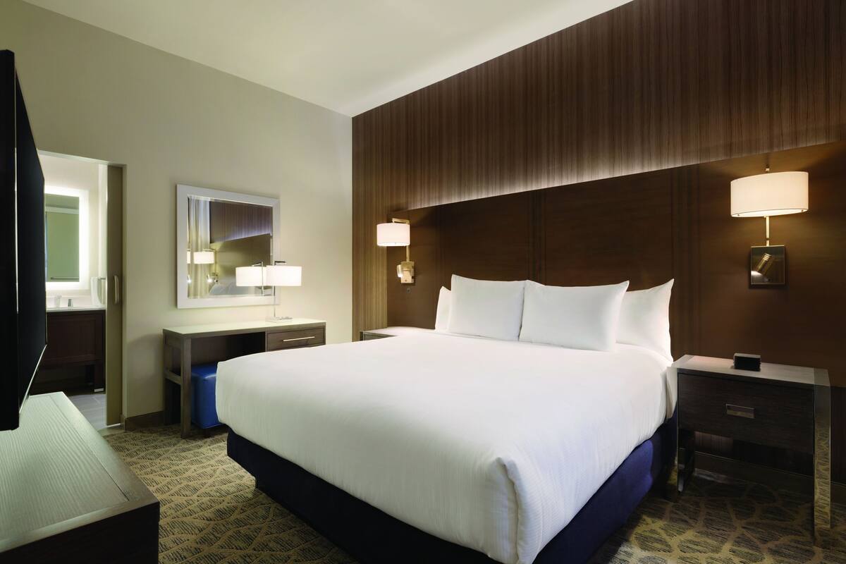 A hotel room with a large bed, bedside tables, a mirror, and a television.