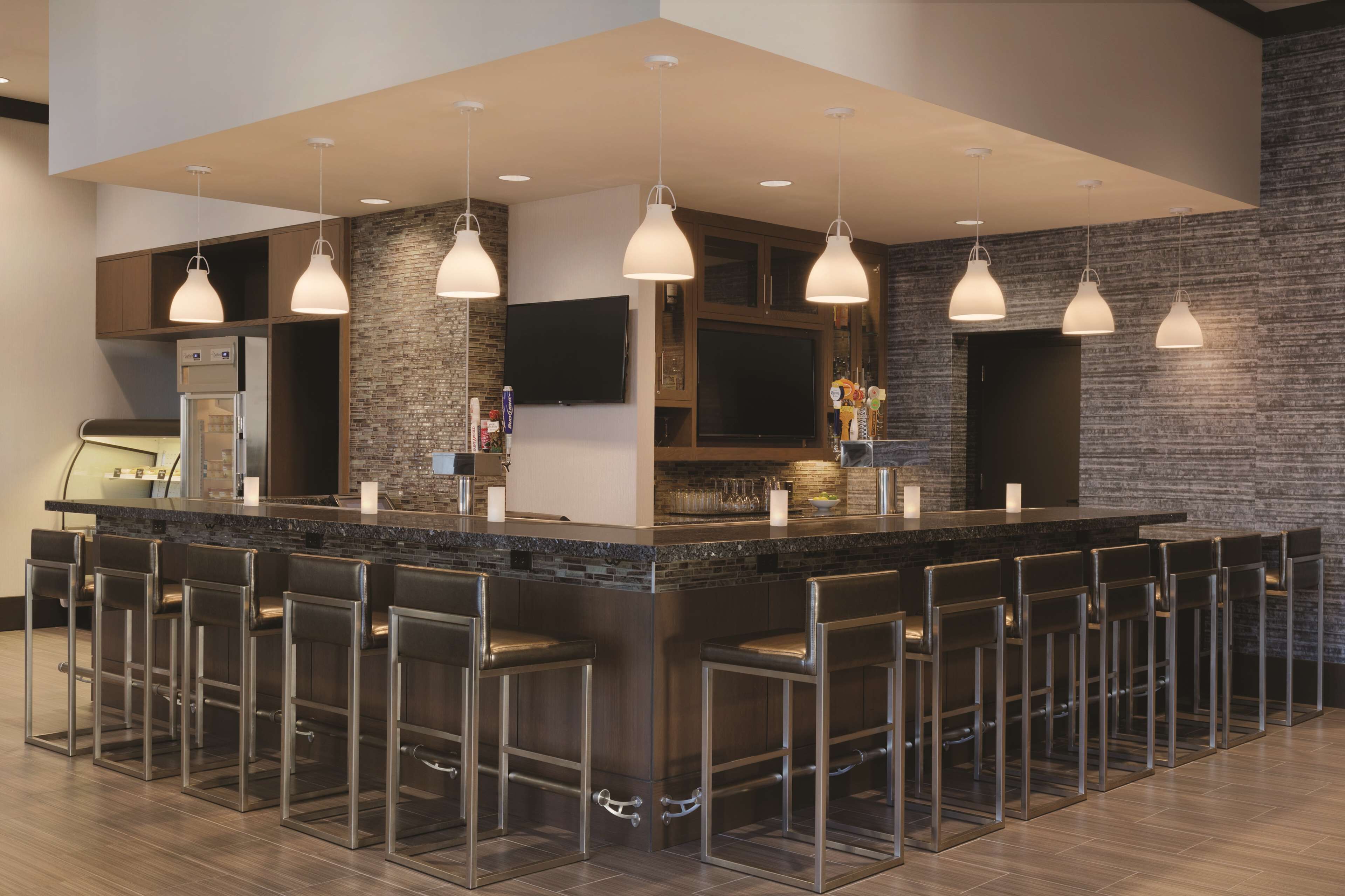 A modern kitchen with a central island, bar stools, pendant lighting, and a flat-screen TV.