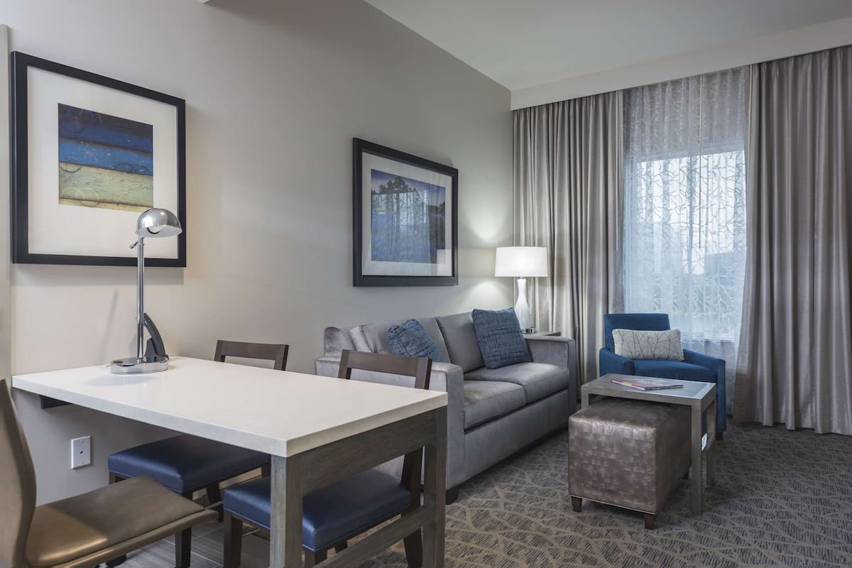 A hotel room with a dining area, a sofa, a chair, and a small table.