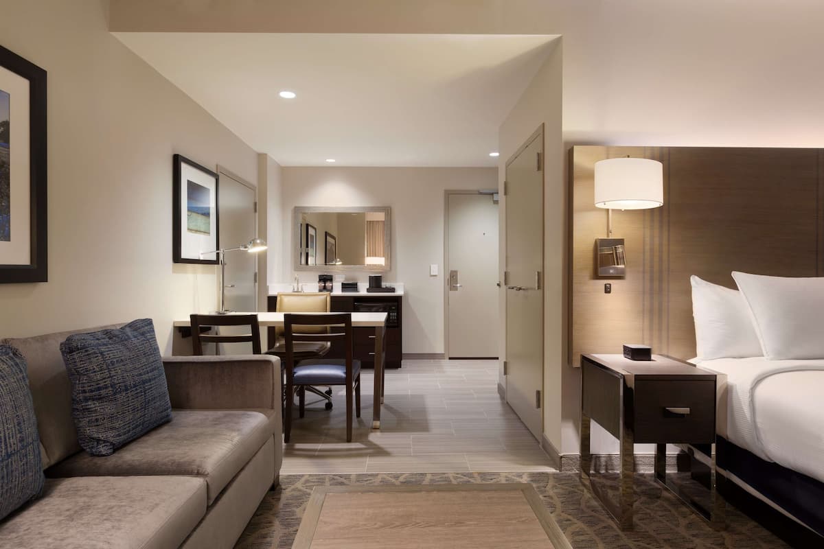 A hotel room with a bed, a desk, a chair, a sofa, and a nightstand.