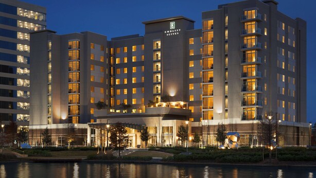 Un hotel de varios pisos con un llamativo letrero de 'Embassy Suites', amplias ventanas y un área ajardinada al frente.