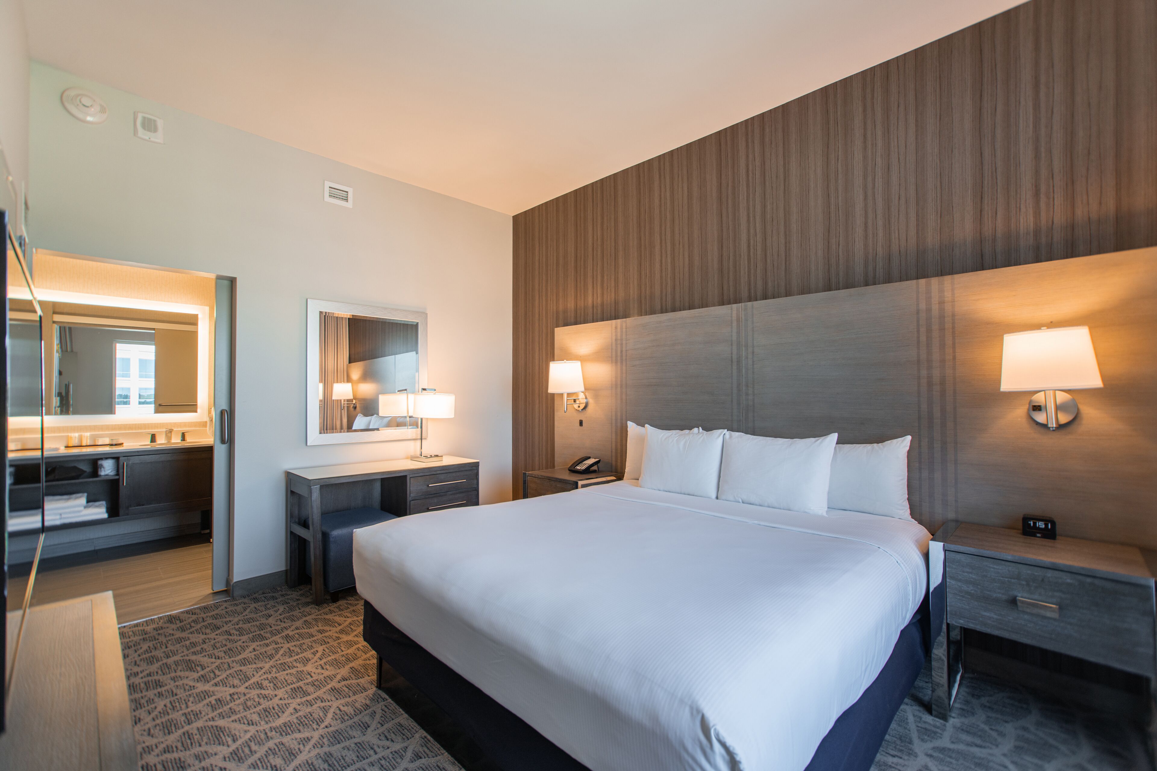 A hotel room with a large bed, bedside tables, a mirror, and a wall-mounted lamp.