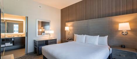 A hotel room with a large bed, bedside tables, a mirror, and a wall-mounted lamp.
