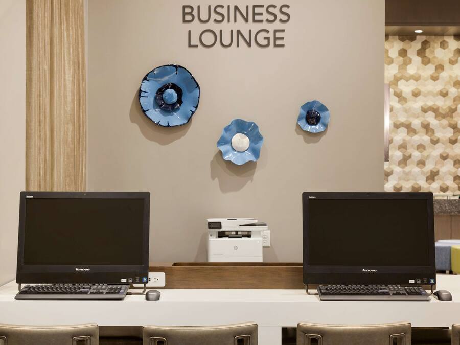 Eine Geschäfts-Lounge mit zwei Lenovo-Laptops, einem Drucker und blauen Dekotellern an der Wand.