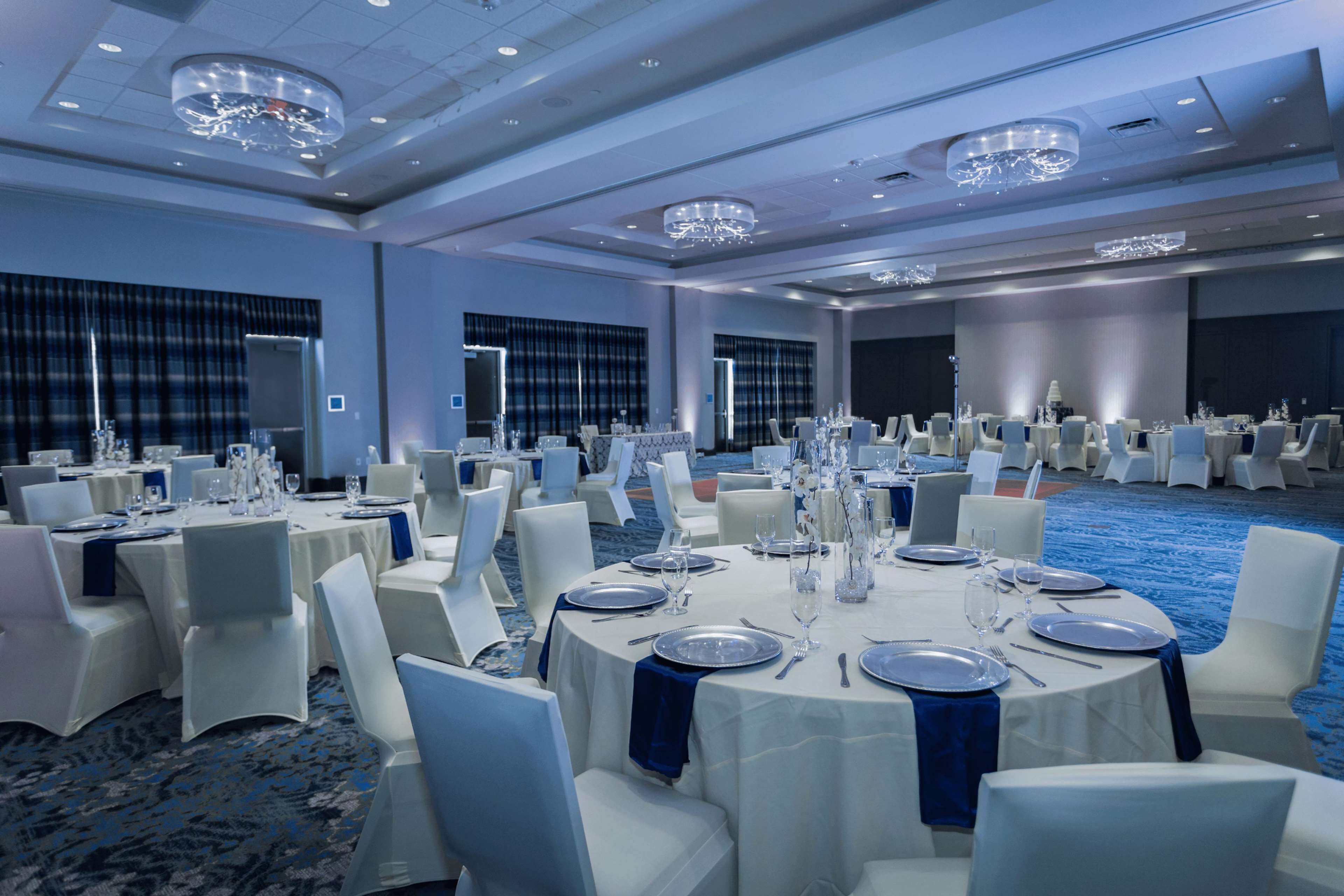 A banquet hall with round tables set for dining, white chairs, and blue tablecloths.