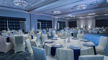 A banquet hall with round tables set for dining, white chairs, and blue tablecloths.