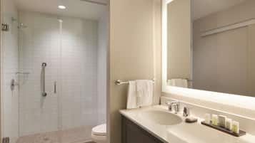 A modern bathroom with a glass-enclosed shower, a white sink with a mirror, and a towel rack.