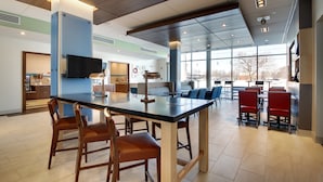 A spacious indoor area with a long counter and several chairs, a television mounted on the wall, and large windows providing natural light.