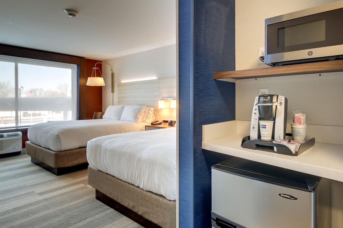 A hotel room with two beds, a kitchenette with a coffee maker, and a view of the outdoors.