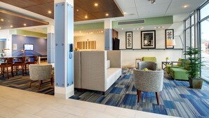 A modern hotel lobby with a seating area, a reception desk, and a large window offering a view.
