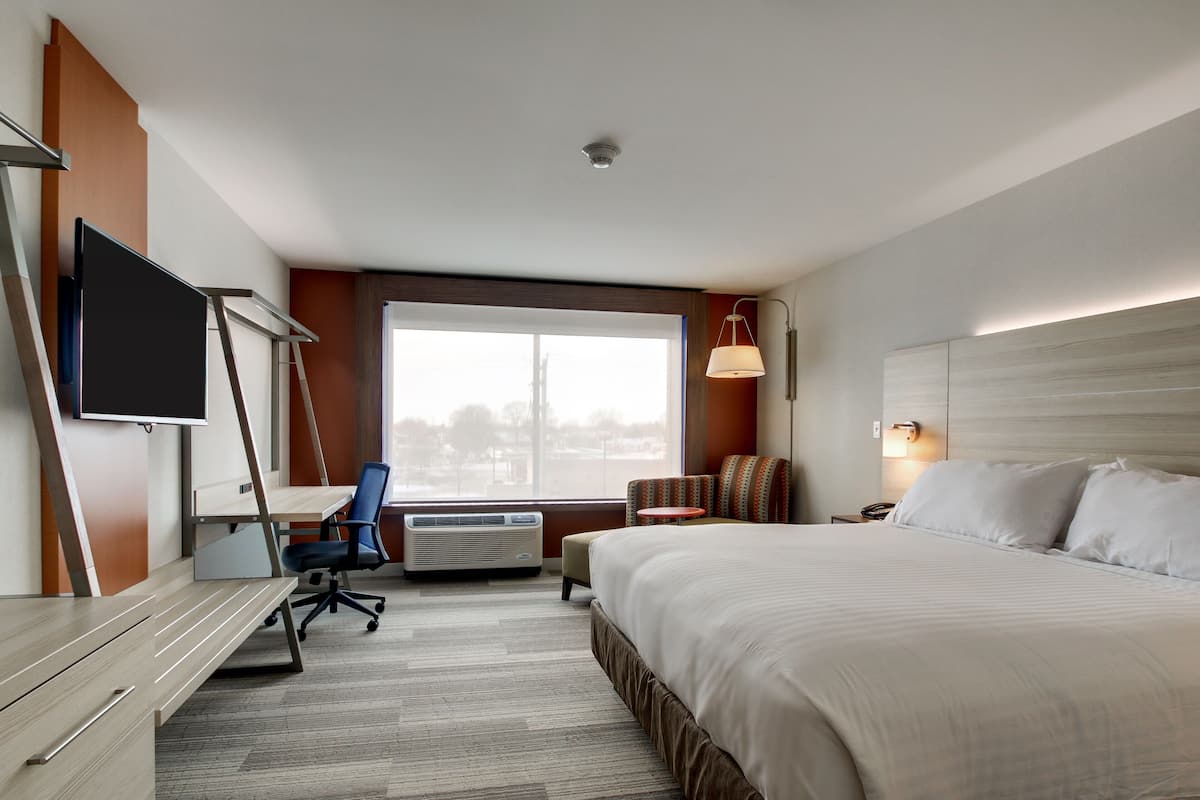 A hotel room with a bed, desk, chair, TV, and a large window.