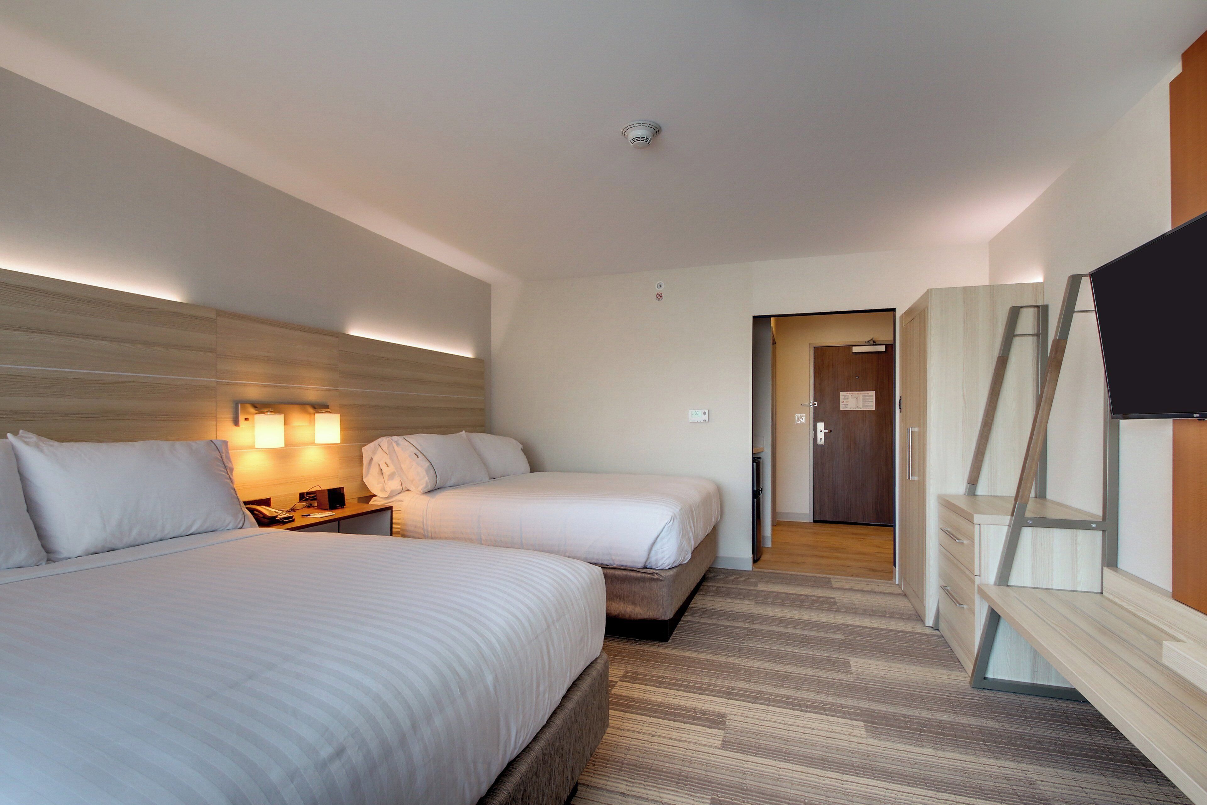 A hotel room with two beds, a desk with a telephone, and a TV mounted on the wall.