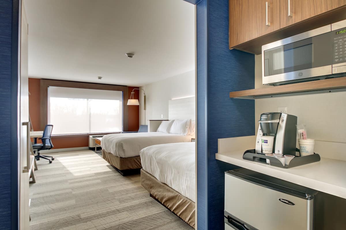 A hotel room with two beds, a desk, a microwave, a coffee maker, and a refrigerator.