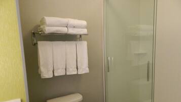 A bathroom with a toilet, a glass shower enclosure, and a towel rack with folded towels.