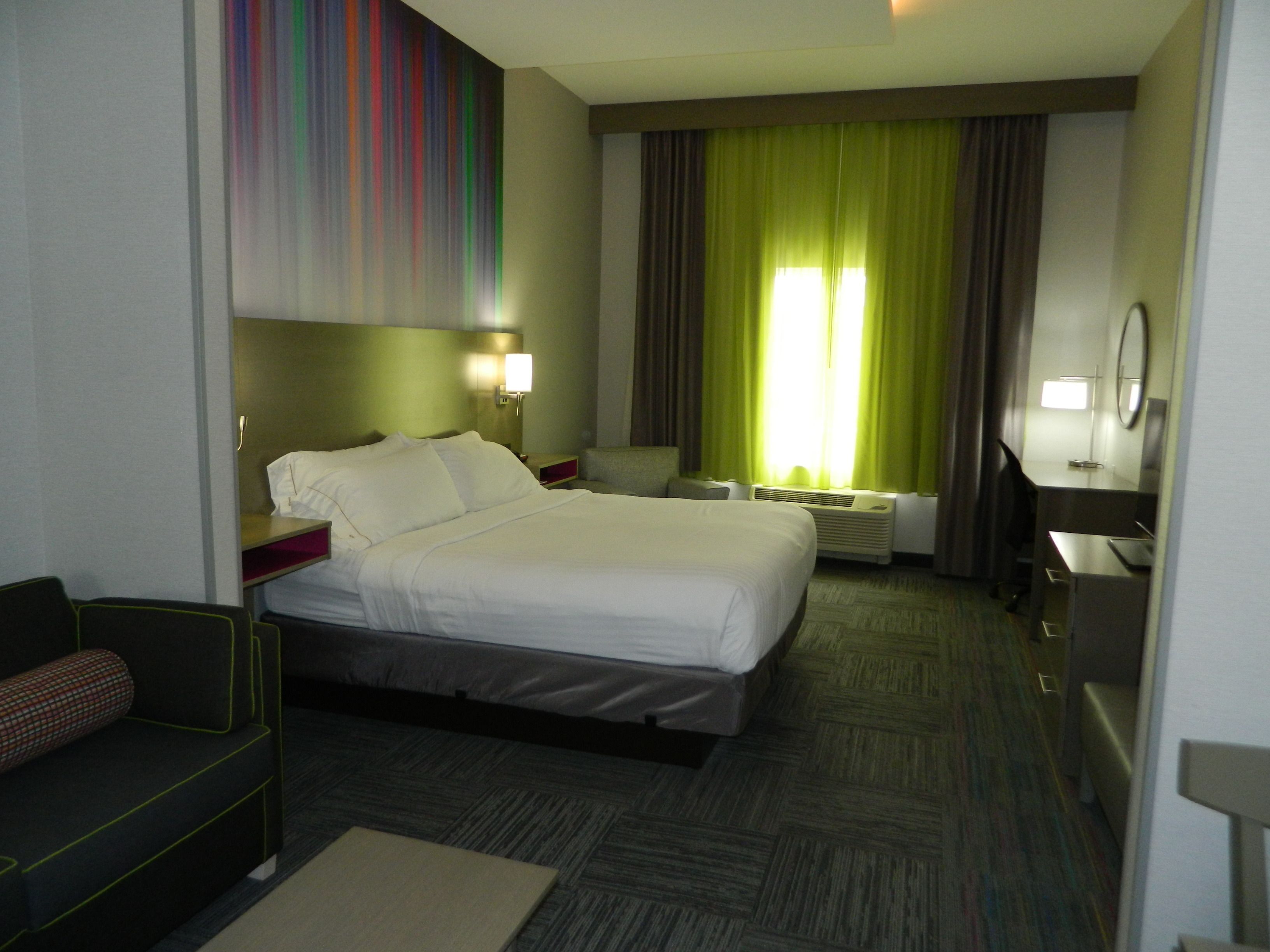 A hotel room with a bed, bedside tables, a desk, a chair, a mirror, and a window with curtains.