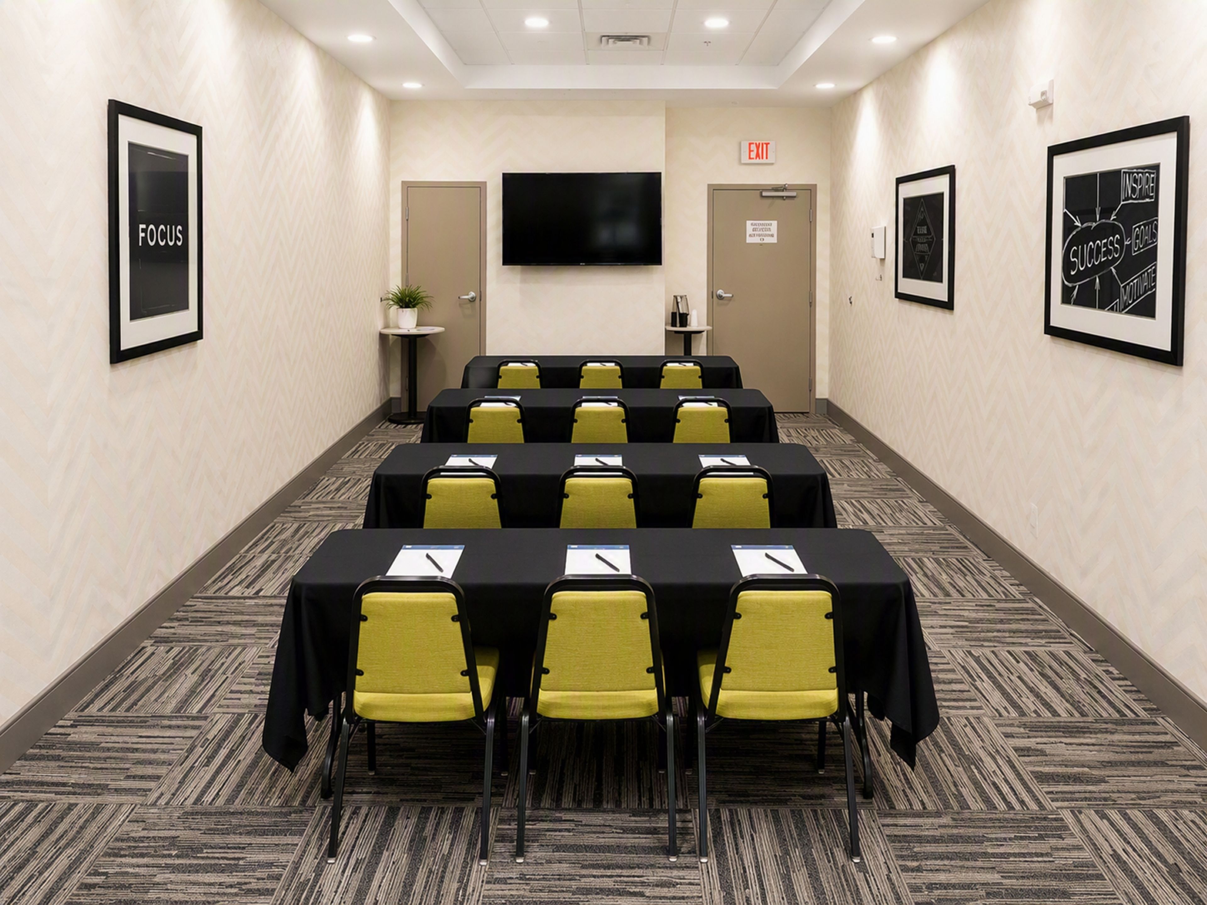 A conference room with tables and chairs, a flat-screen TV on the wall, and framed motivational posters.