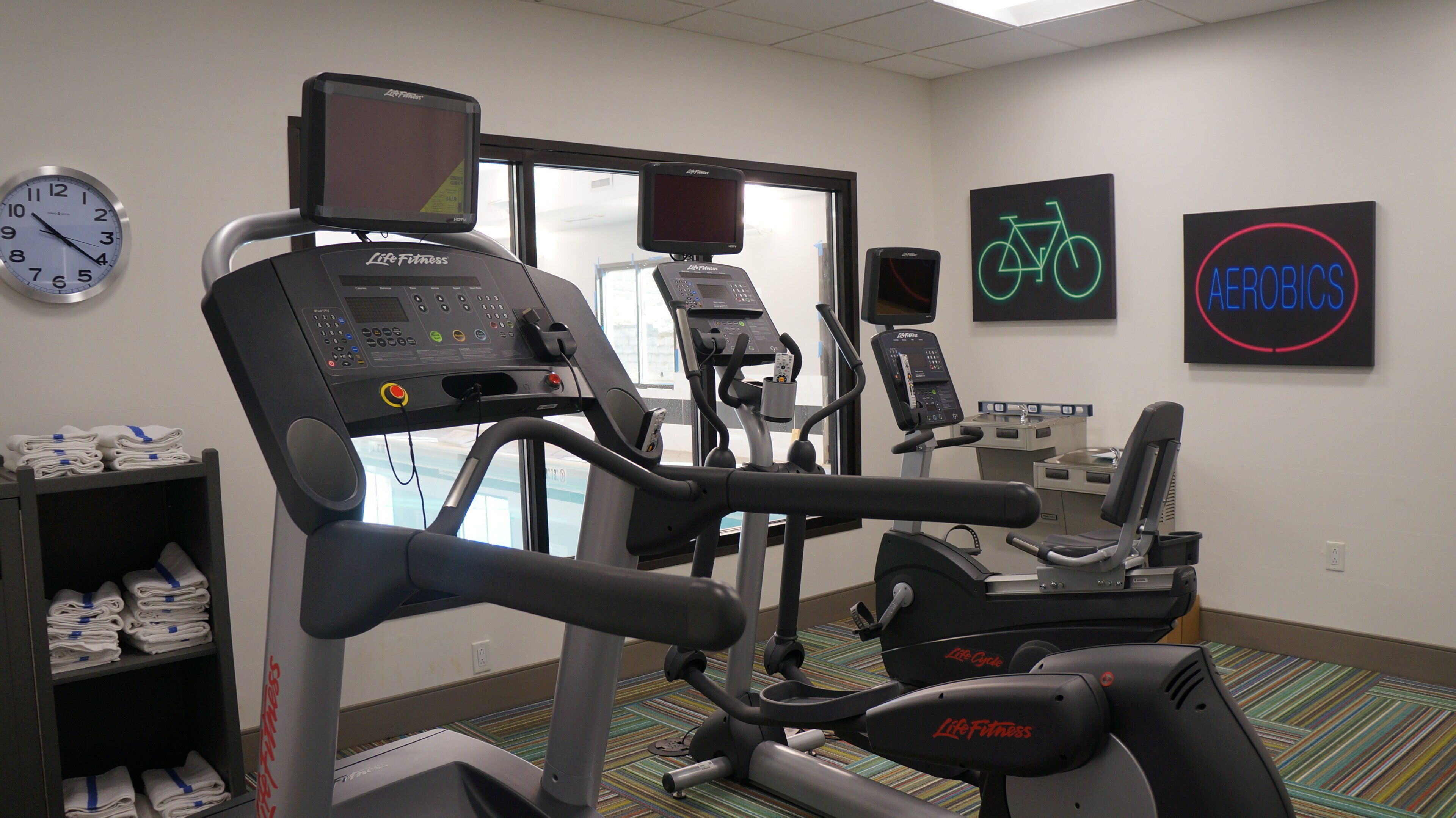 A gym with treadmills, stationary bikes, and a wall clock.