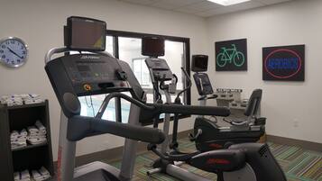 Un gimnasio con cintas de correr, bicicletas estáticas y un reloj de pared.