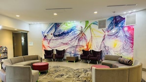 Een moderne lobby met een groot abstract schilderij, comfortabele zitplaatsen en een betegelde vloer.