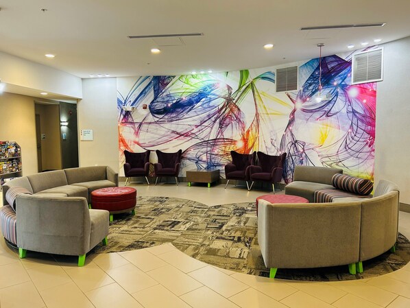 Eine moderne Lobby mit einer großen, abstrakten Wandmalerei, bequemen Sitzmöglichkeiten und einem Fliesenboden.