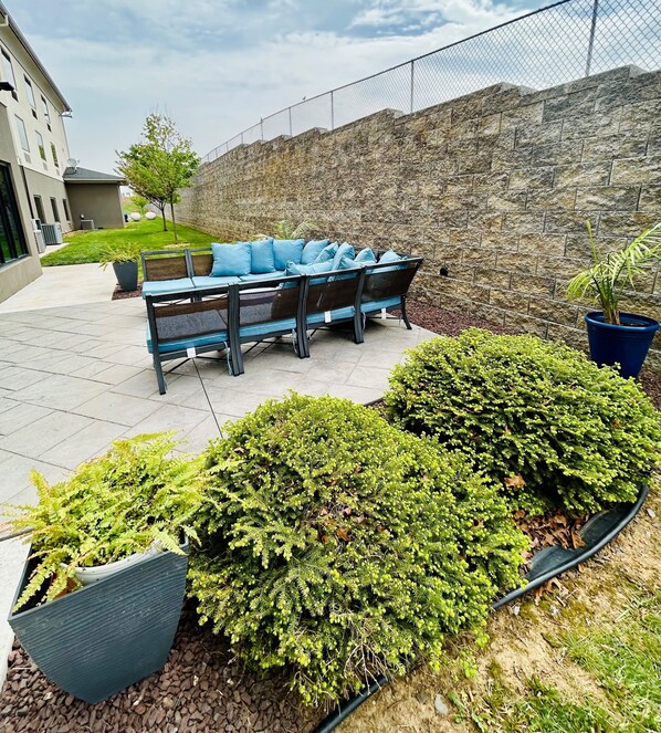 An outdoor seating area with a stone wall, a fence, and potted plants. - Holiday Inn Express & Suites Shippensburg by IHG (Shippensburg)