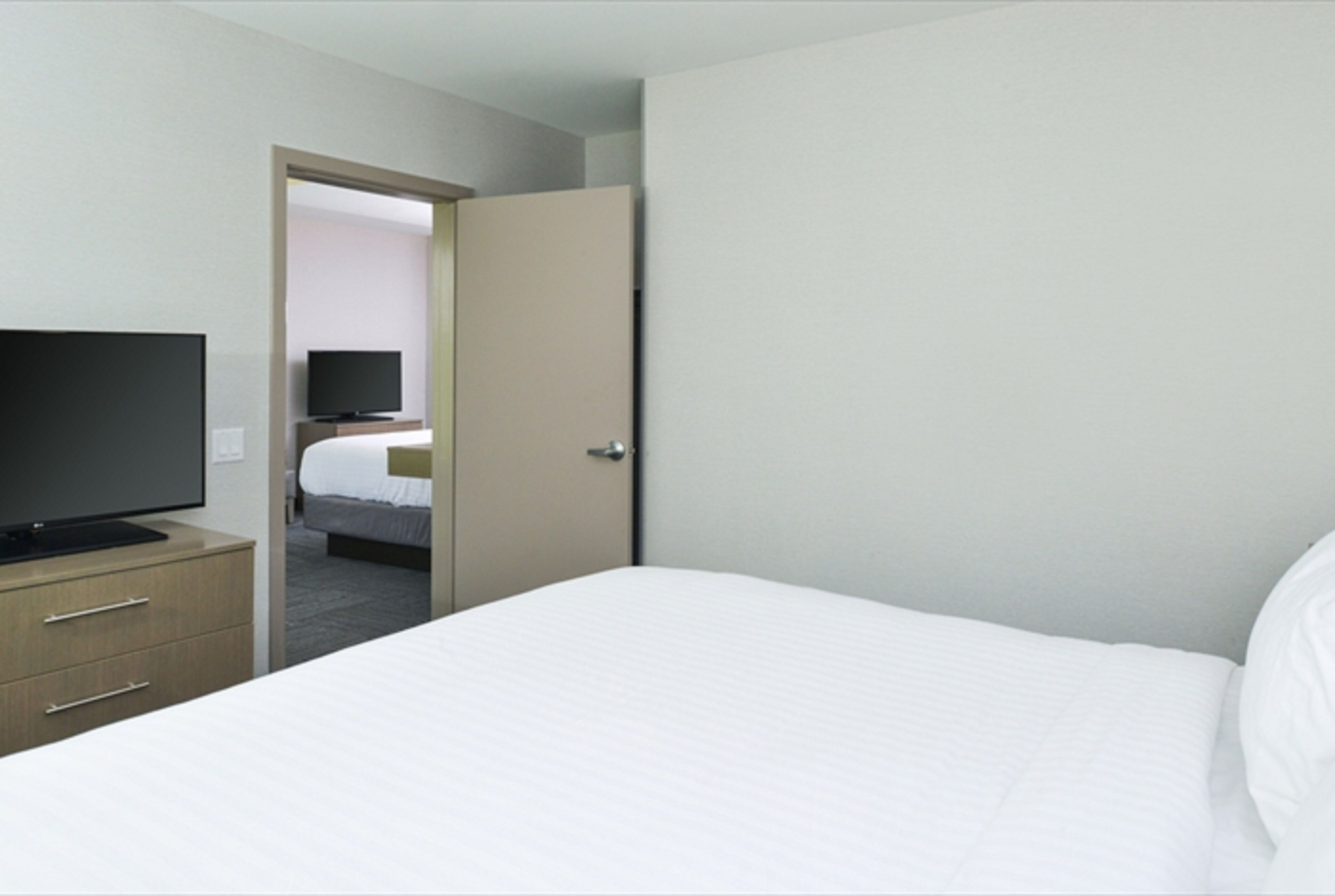 Une chambre d’hôtel avec un lit, un téléviseur posé sur une commode et une porte donnant sur une autre pièce.