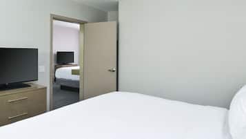 Une chambre d’hôtel avec un lit, un téléviseur posé sur une commode et une porte donnant sur une autre pièce.