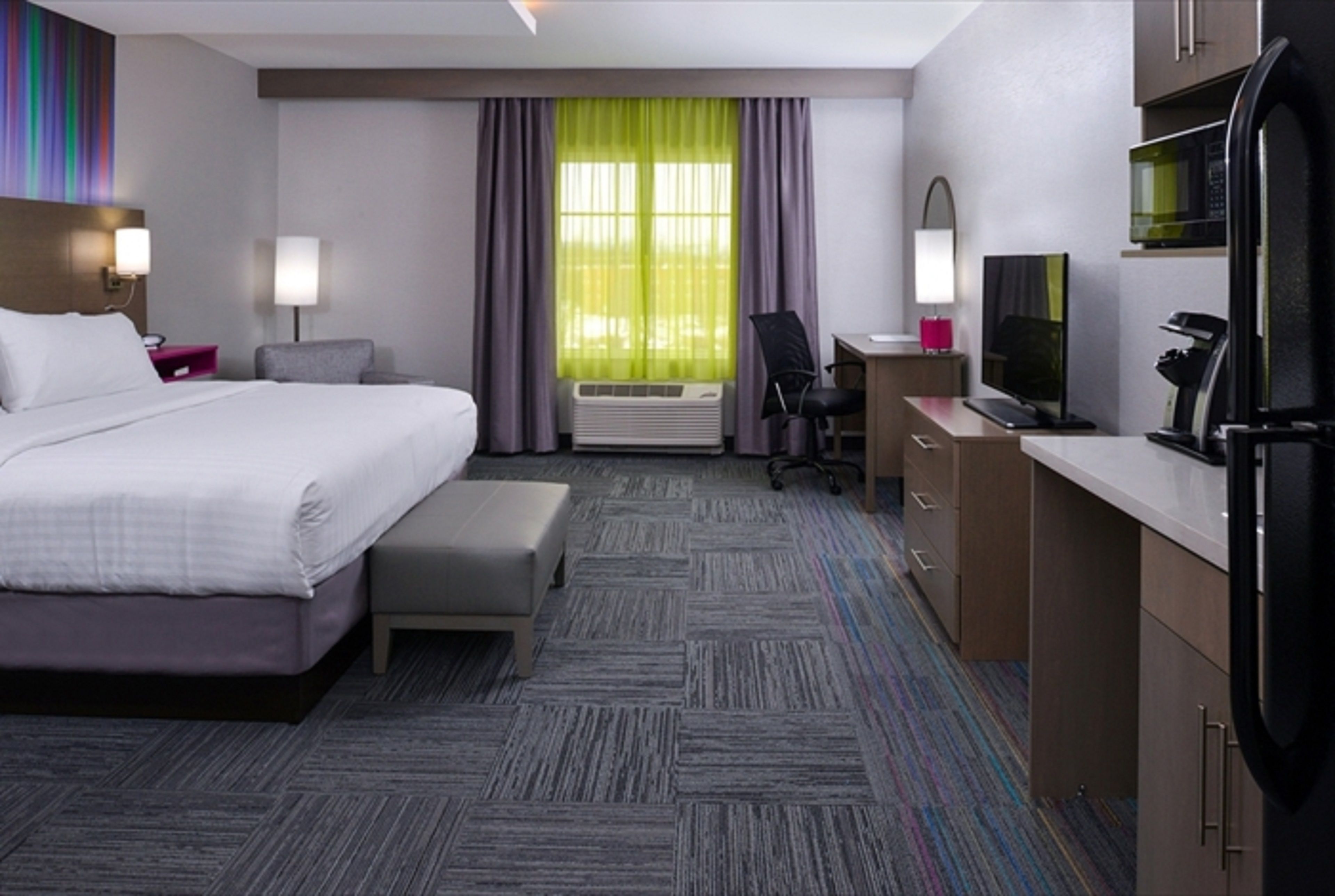 A hotel room with a bed, desk, chair, and kitchenette.