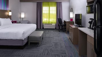 A hotel room with a bed, desk, chair, and kitchenette.