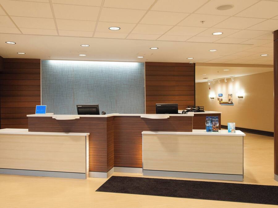 A reception area with two reception desks, a large wall with a textured design, and a series of lights on the ceiling.