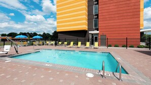 Une piscine avec une terrasse carrelée, un bâtiment jaune et rouge en arrière-plan, et des chaises longues jaunes.