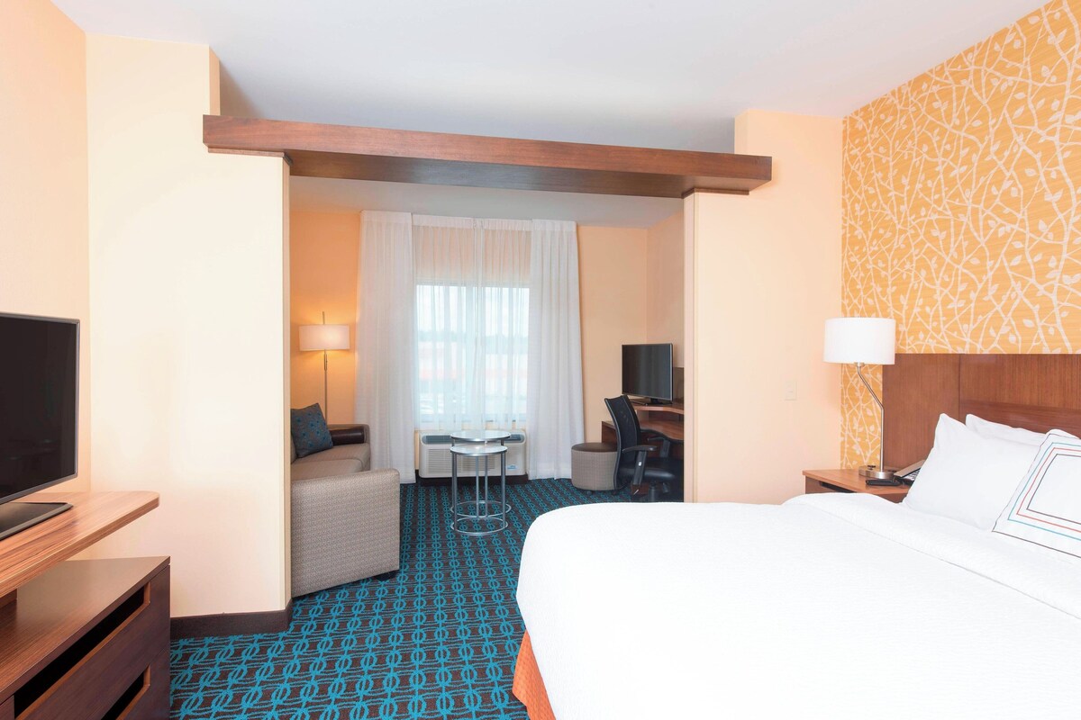 A hotel room with a bed, a desk, a chair, a television, and a window with curtains.