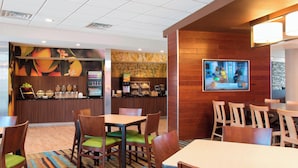 Un espace restaurant avec des tables et des chaises en bois, un comptoir avec un distributeur de boissons et un écran de télévision fixé au mur.