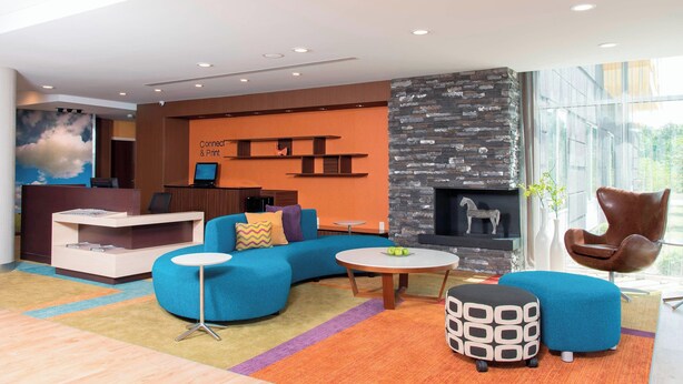 Un hall d’hôtel moderne avec un comptoir d’accueil, un canapé bleu, une table basse ronde et une cheminée.