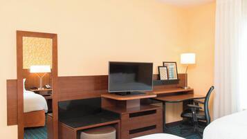 A hotel room with a bed, a desk with a TV, a chair, and a lamp.