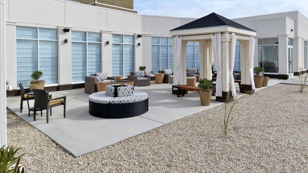 A covered outdoor seating area with multiple sofas and chairs, a central round seating area, and potted plants. - Hilton Garden Inn Hobbs (Hobbs)