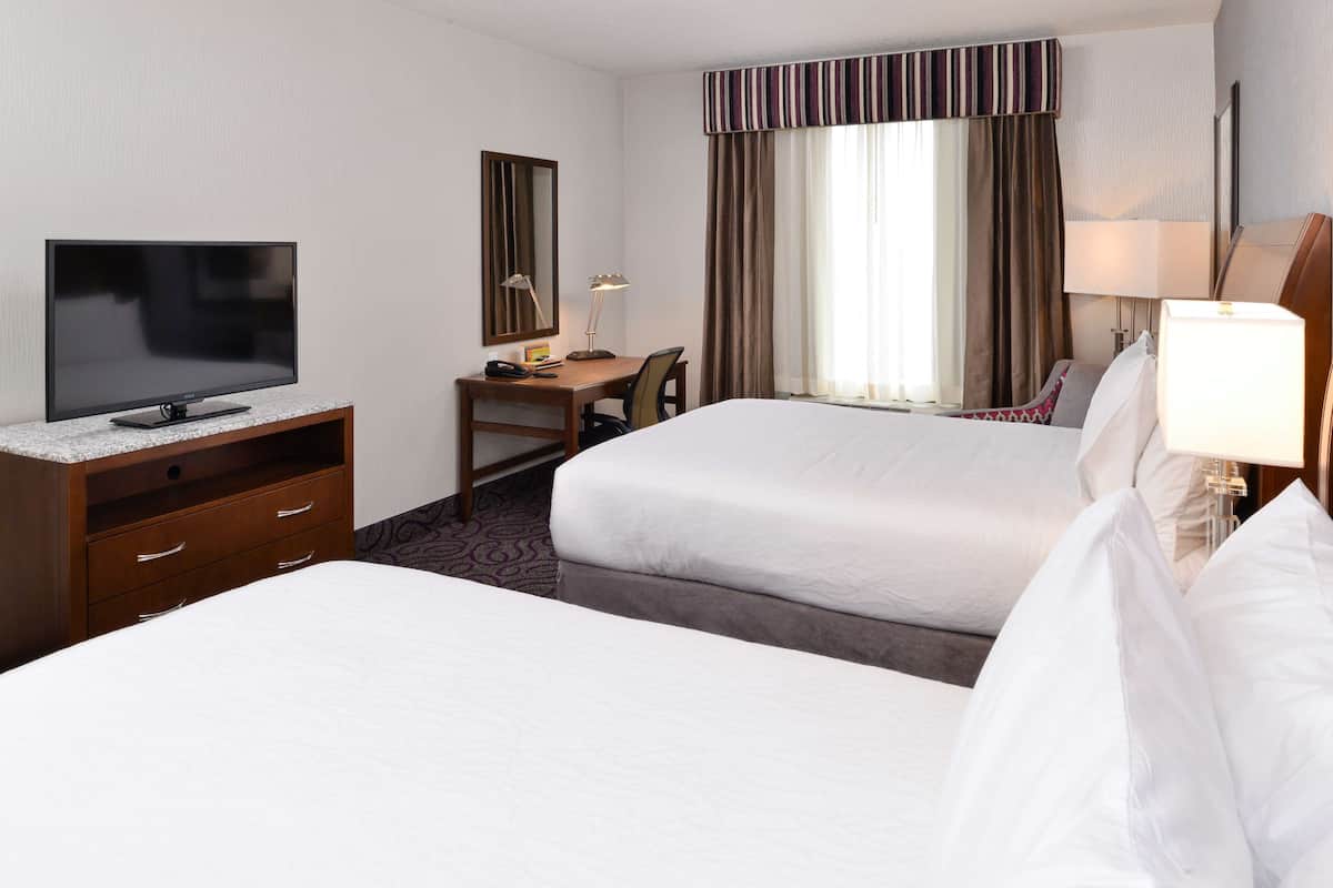 A hotel room with two beds, a desk with a TV, a chair, and a window with curtains.