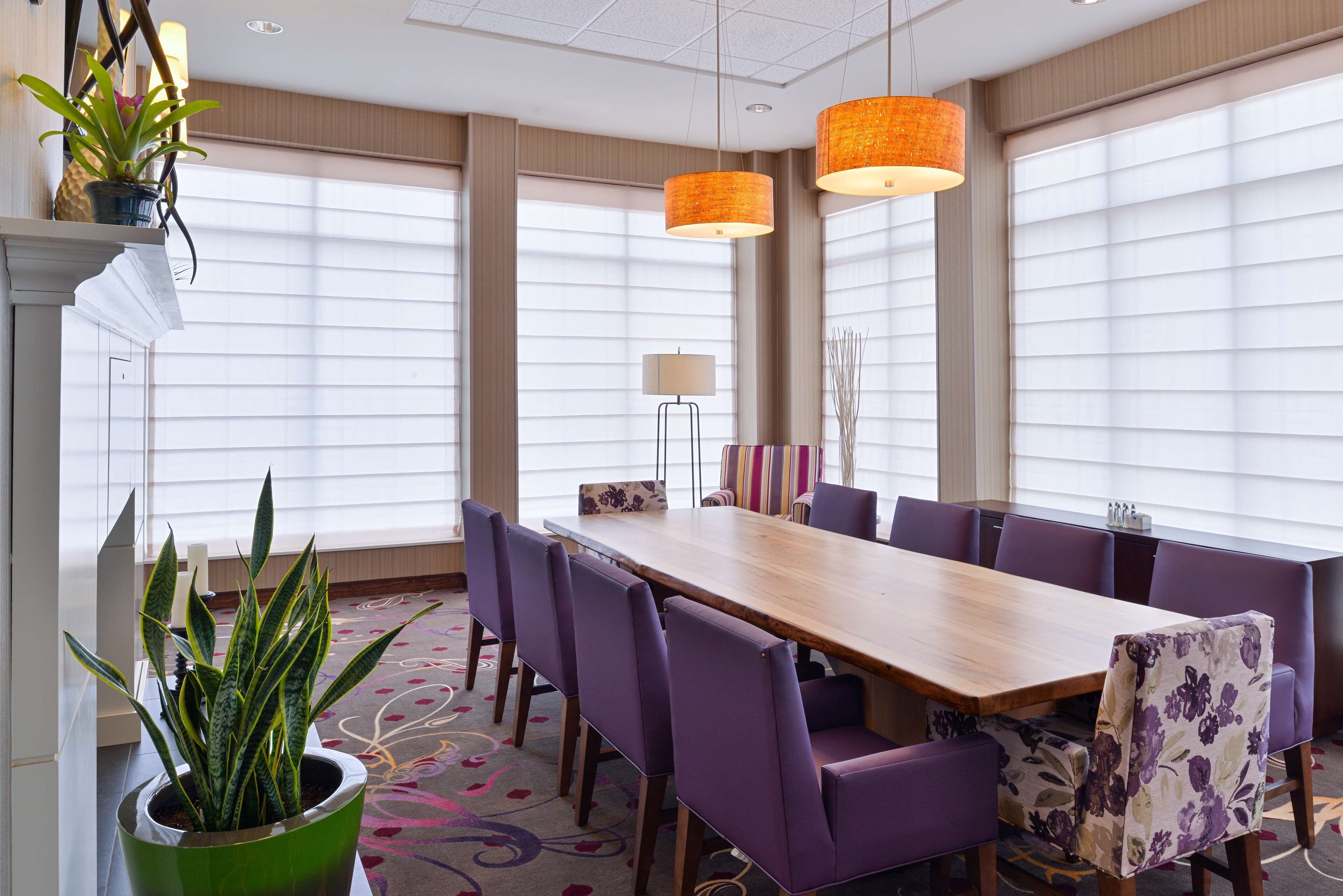 A conference room with a long table, purple chairs, and two orange pendant lights.