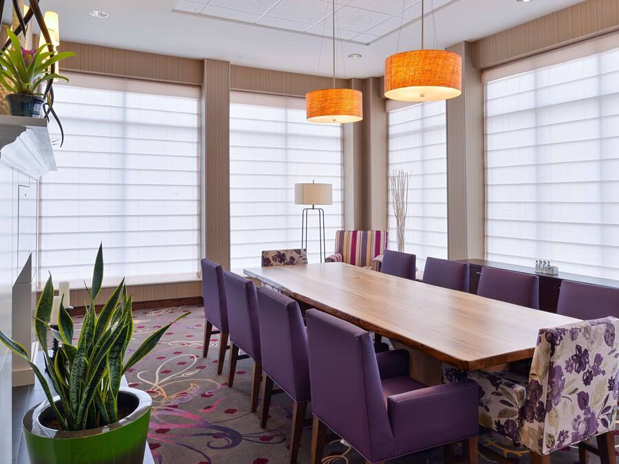 A conference room with a long table, purple chairs, and two orange pendant lights.