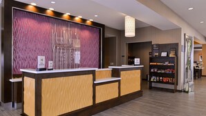 A reception area with a modern design, featuring a reception desk, a decorative wall, and a bookshelf with various items. - Hilton Garden Inn Hobbs (Hobbs)