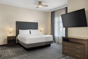 Ein Hotelzimmer mit Bett, Flachbildfernseher, Deckenventilator und einem Fenster mit Vorhängen.